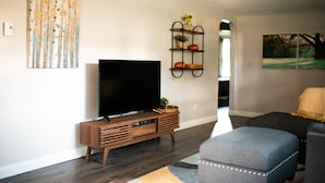 Un soggiorno moderno con una TV a schermo piatto su un supporto in legno, un divano nero e un poggiapiedi grigio con luci a LED.