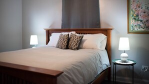 Un letto rifatto con cura, una testiera in legno, due lampade ai lati del letto e un quadro con dei fiori al muro.