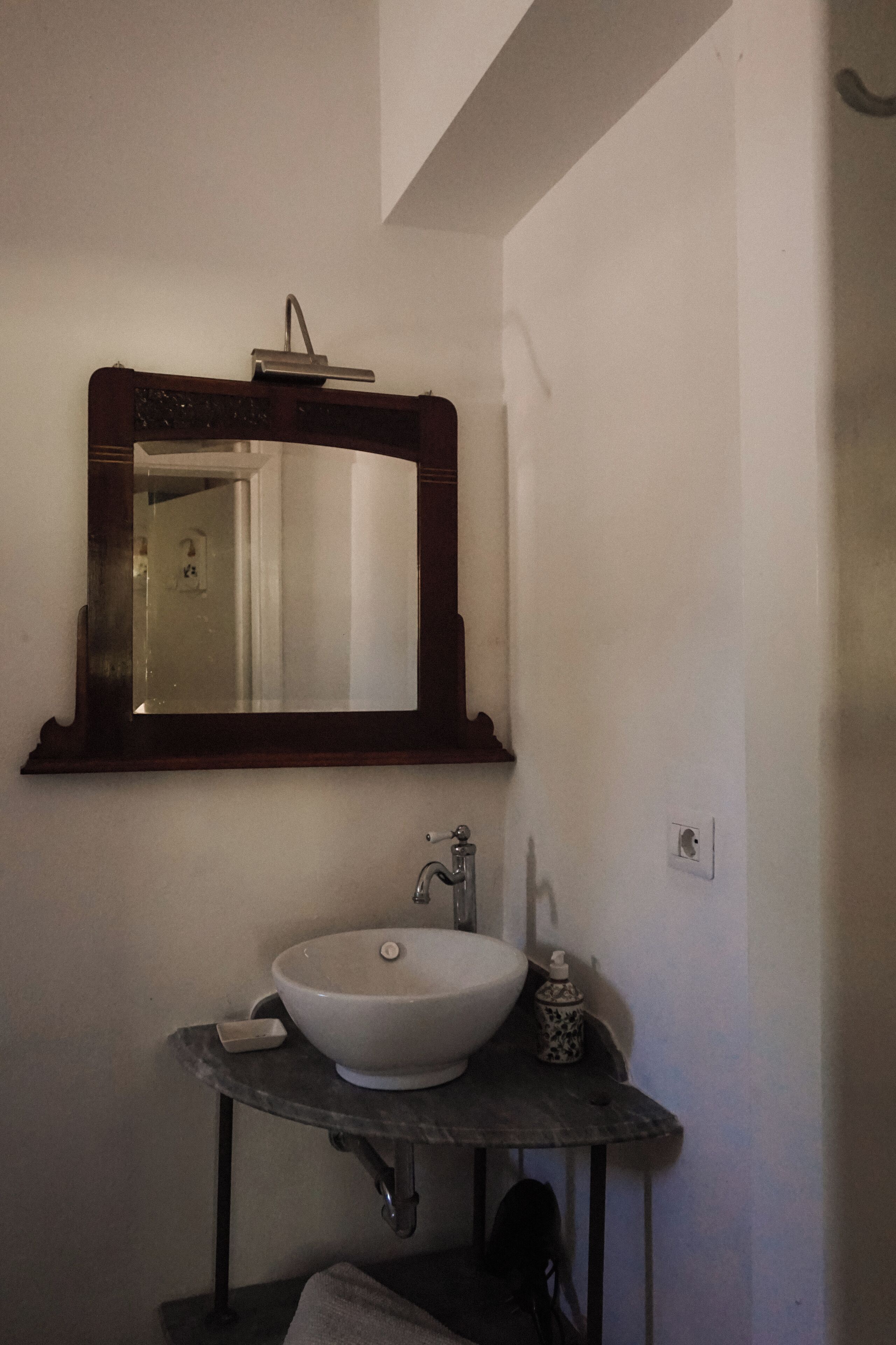 Un bagno con un lavandino bianco, uno specchio con cornice in legno e un piccolo tavolo con dispenser di sapone.