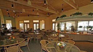 A spacious indoor area with round tables and wicker chairs, featuring a high ceiling with exposed beams and large windows allowing natural light. - Absolutely Pristine 2-2 Lower Unit with Stunning Views! 2027 BNP Paribas Close!! (La Quinta)