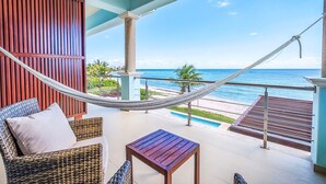 A balcony with a hammock, wicker furniture, and a view of the ocean. - Luxurious and elegant beachfront villa with a heated pool! (Akumal)