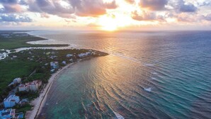 An aerial view of a coastal area with a beach, buildings, and the ocean. - Luxurious and elegant beachfront villa with a heated pool! (Akumal)