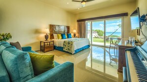 A bedroom with a bed, a desk, a piano, and a view of the ocean. - Luxurious and elegant beachfront villa with a heated pool! (Akumal)