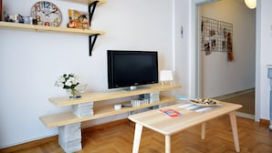 Ein Wohnzimmer mit Flachbildfernseher, Holzregalen, einer Betonbank, einem kleinen Tisch und einem Blumenvasen.