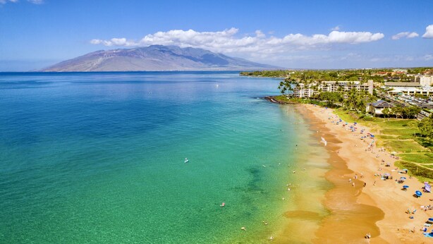 A coastal view with a beach, clear water, and a mountain in the background. - Maui Banyan P304 - Remodeled, Partial Ocean View, AC, Across from Kamaole Beach! (Kihei)