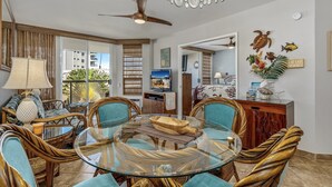 A dining area with a glass table, wicker chairs, and a ceiling fan. - Maui Banyan P304 - Remodeled, Partial Ocean View, AC, Across from Kamaole Beach! (Kihei)