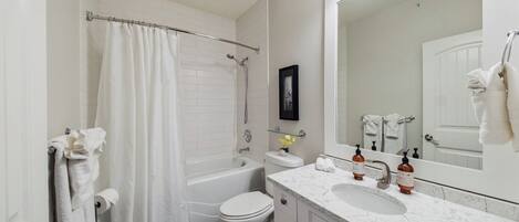 A bathroom with a bathtub, toilet, and a large mirror.