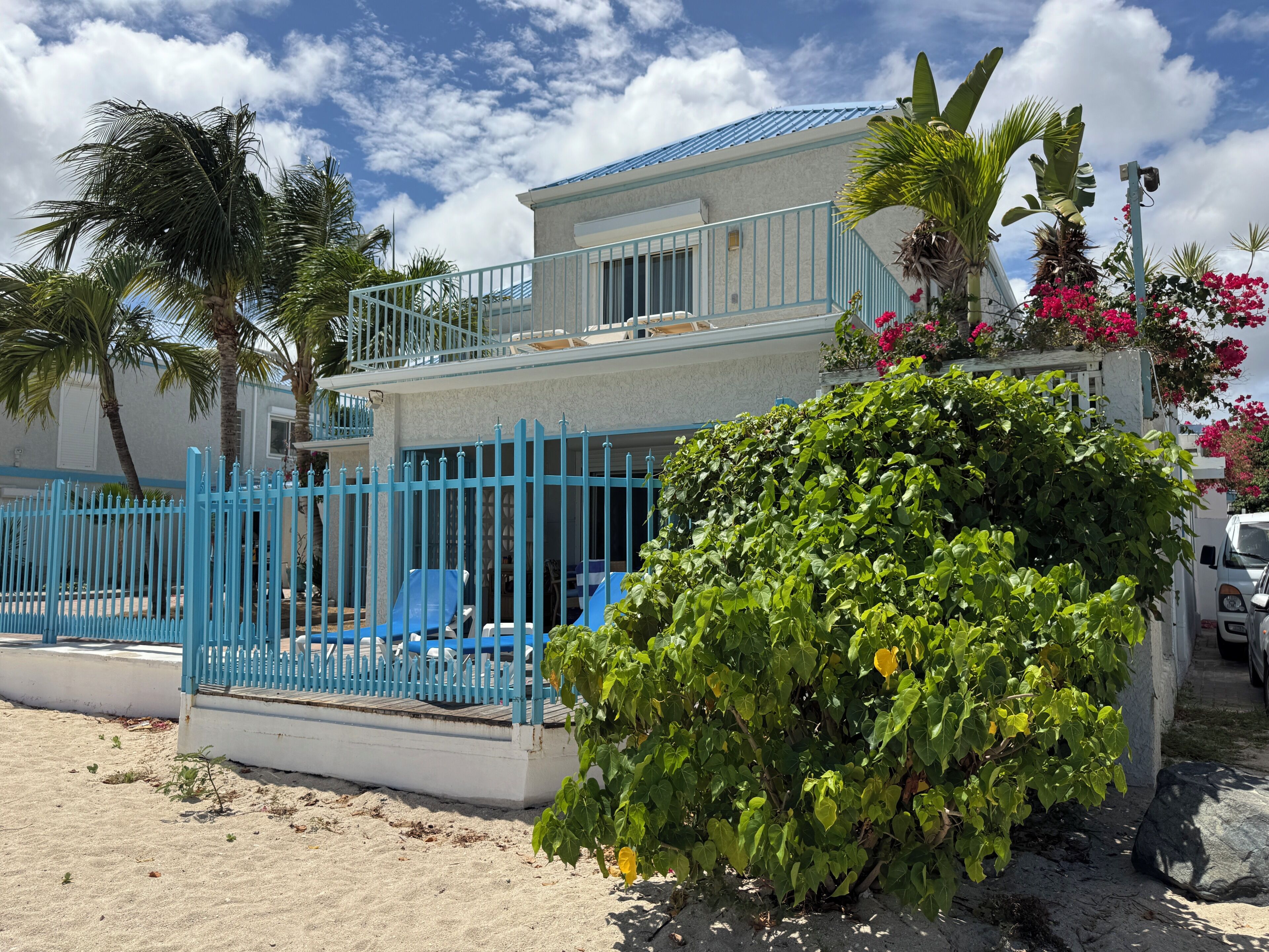 A two-story building with a blue fence, a balcony, and a garden area with plants and flowers.