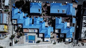 Un hotel frente a la playa con varios edificios de techos azules, una piscina y una playa de arena.