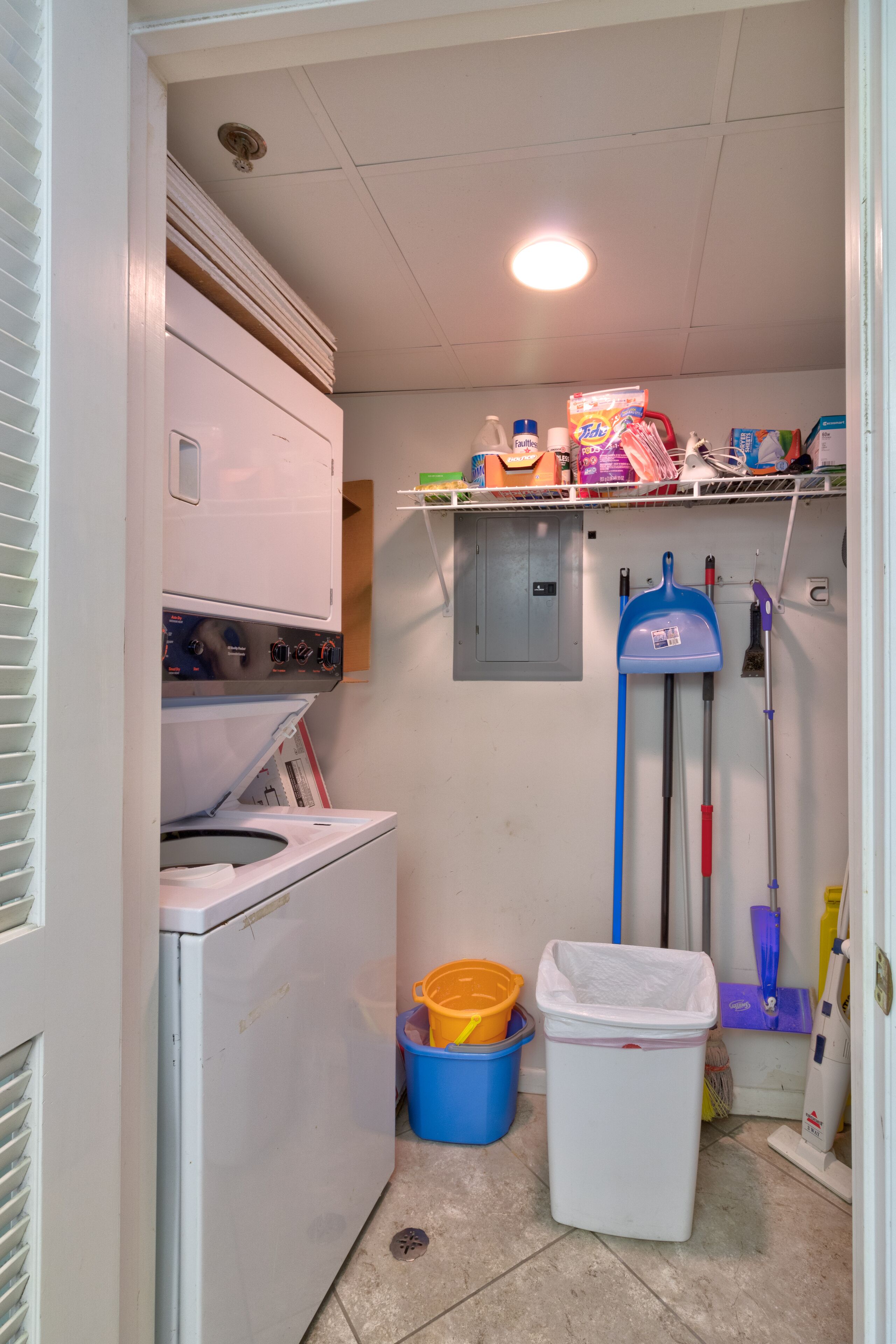 A laundry room with a washing machine, a drying rack, a mop, a broom, and cleaning supplies.