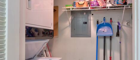 A laundry room with a washing machine, a drying rack, a mop, a broom, and cleaning supplies.