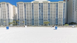 A high-rise hotel with multiple balconies, a flat roof, and a sandy beach in the foreground.