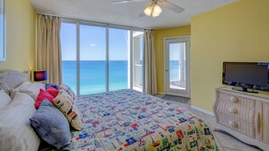 A bedroom with a bed, a television, a ceiling fan, and a view of the ocean.