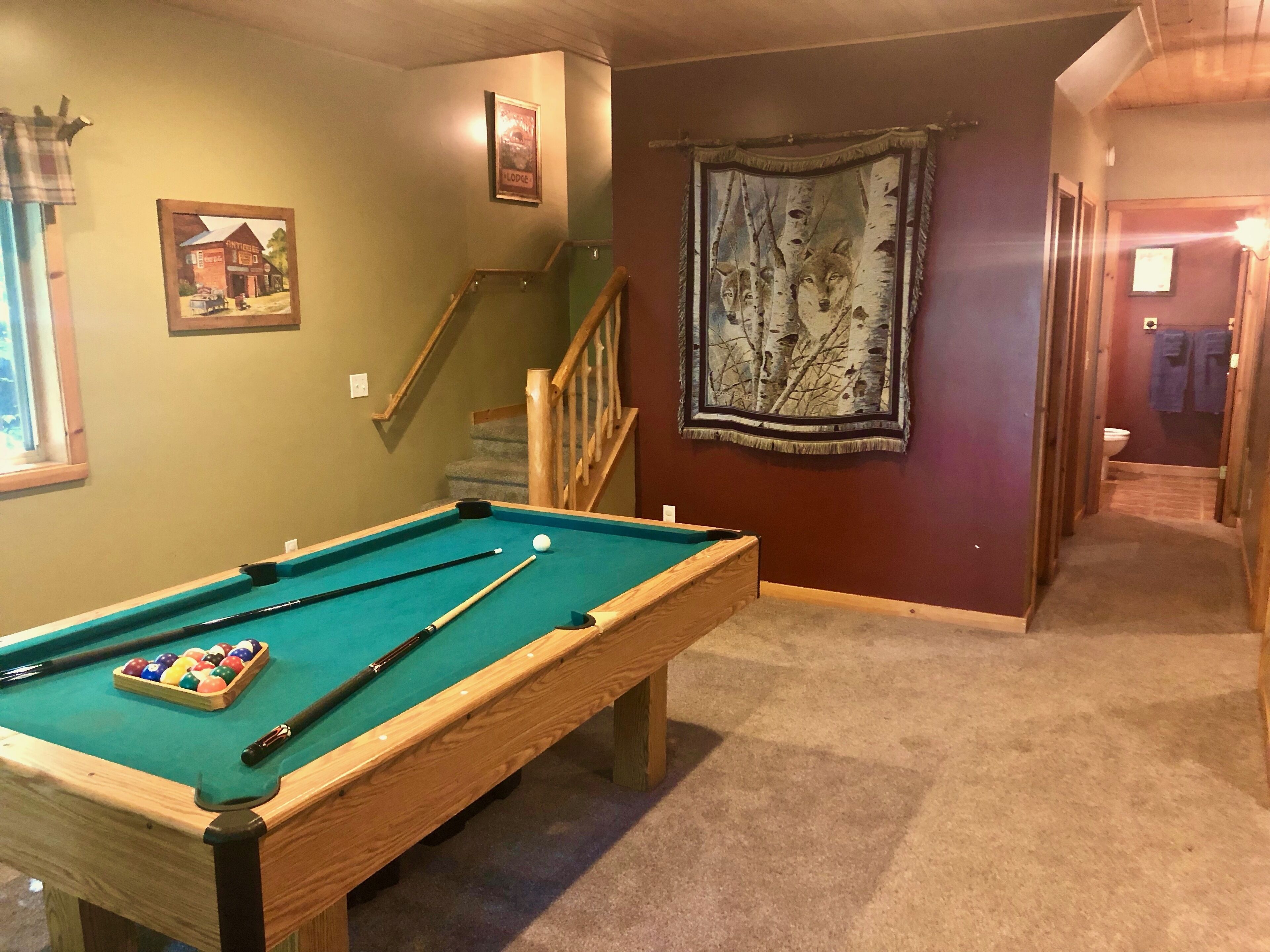Een pooltafel met ballen en stokken, een trap en een gang met een wandtapijt en een deur.
