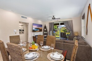 Comedor con una mesa preparada para cuatro personas, rodeado de sillas de mimbre, un ventilador de techo y vistas al exterior.
