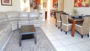Una sala de estar moderna con un sofá modular, una mesa de comedor con sillas y una cocina al fondo.