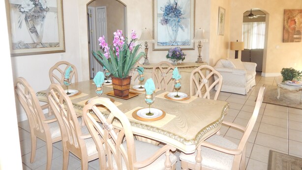 Un comedor con una mesa dispuesta para seis personas, rodeada de sillas de madera, un candelabro y cuadros en las paredes.