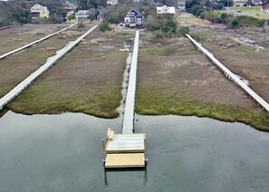 Une propriété située au bord de l’eau, avec une jetée qui s’avance sur l’étendue d’eau, entourée de pelouses et de quelques maisons en arrière-plan.