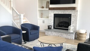 Ein modernes Wohnzimmer mit einer schwarzen Ledersofa, blauen Ohrensesseln, einem Holztisch und einem Kamin.