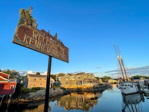 Una propiedad frente al agua con un cartel que dice 'Welcome to Pine Bunkport', un muelle con barcos y una hilera de casas.