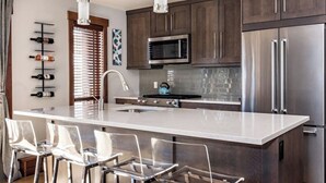 A modern kitchen with a central island, stainless steel appliances, and a wine rack. - Minutes to festivals - Pool, Jacuzzi, Fitness room (Snowmass Village)