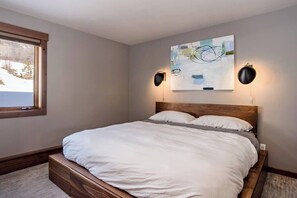 Un dormitorio con una cama de madera, una ventana y un cuadro abstracto colgado en la pared.