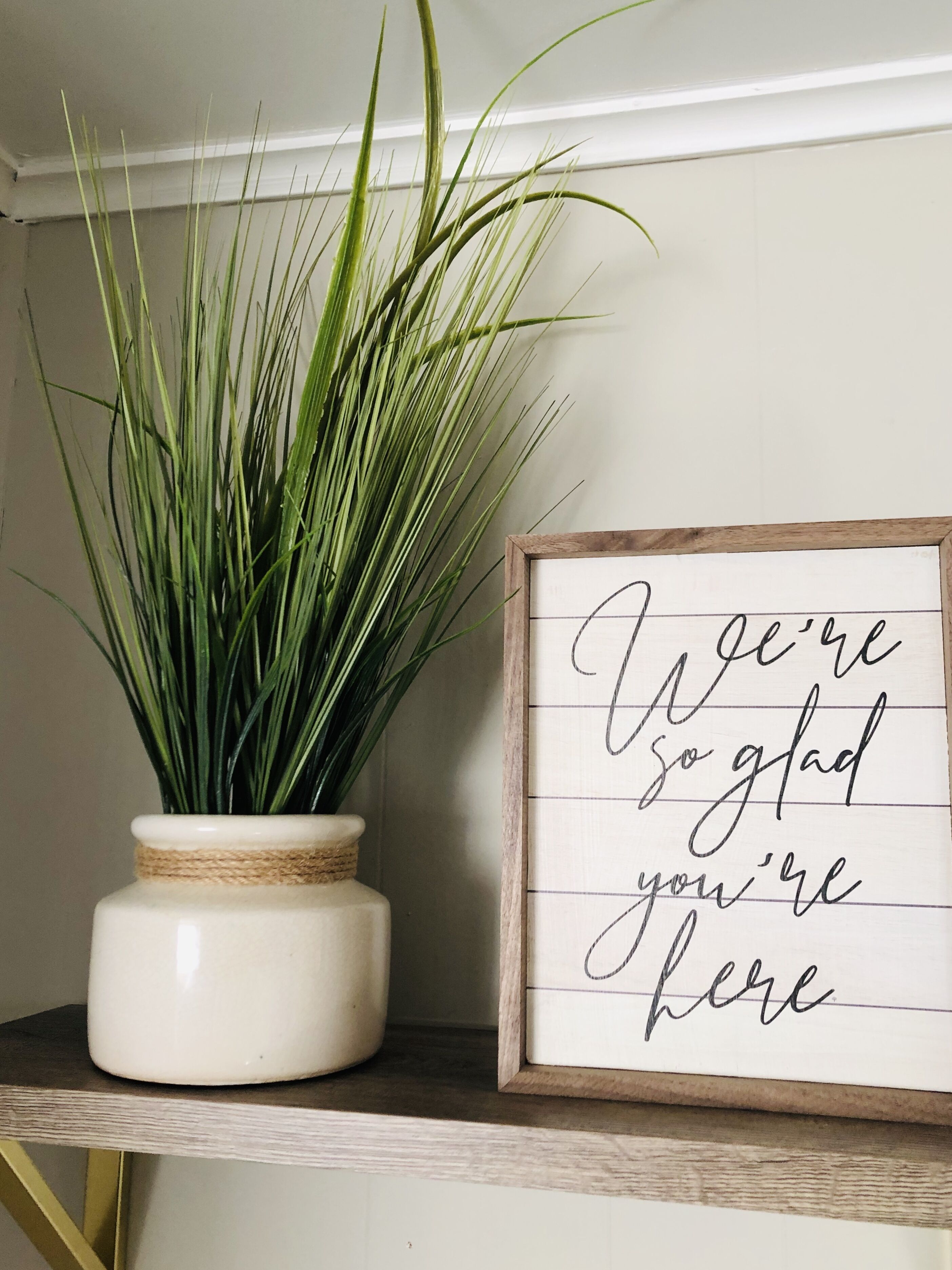 A framed sign with a handwritten message, a potted plant, and a shelf.