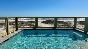 A rectangular swimming pool with clear blue water, surrounded by a wooden deck and a metal fence. - Amazing Views! Beachfront Home Sleeps 16-Private Pool & Private Beach! (Gulf Shores)