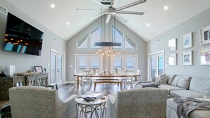 A spacious living area with a high ceiling fan, a large TV, and a dining table set for six. - Amazing Views! Beachfront Home Sleeps 16-Private Pool & Private Beach! (Gulf Shores)