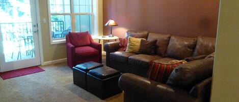 Ein Wohnzimmer mit einem braunen Ledersofa, einem roten Sessel und einem kleinen Tisch mit einer Lampe.