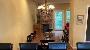 A spacious kitchen with granite countertops, a dining area with a wooden table and chairs, a stone fireplace, and a view through the glass door. - Ideal location in Collins Lake, close to pool with views of Forest & the Slopes (Government Camp)