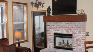A living room with a brick fireplace, a ceiling fan, and a flat-screen TV mounted above it. - MILLION DOLLAR VIEW! 4 Bedrooms all with Private Bathroom, Great Dock 16X36 Slip (Sunrise Beach)