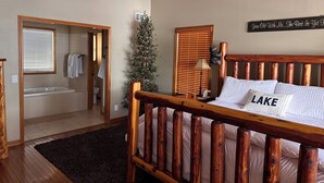 A bedroom with a wooden bed, a small Christmas tree, a sign on the wall, and a view into the bathroom. - MILLION DOLLAR VIEW! 4 Bedrooms all with Private Bathroom, Great Dock 16X36 Slip (Sunrise Beach)
