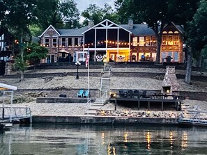 Ein Anwesen am Wasser mit einem großen Gebäude, das zahlreiche Fenster und einen überdachten Bereich mit Lichterketten aufweist.