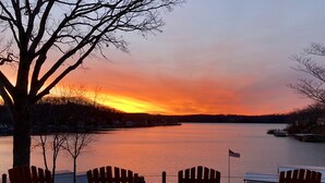 A sunset view from a lakeside deck with three wooden Adirondack chairs and a flag. - MILLION DOLLAR VIEW! 4 Bedrooms all with Private Bathroom, Great Dock 16X36 Slip (Sunrise Beach)