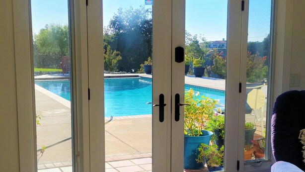 A view through a glass door to a swimming pool area with potted plants and a clear sky. - MYSTICAL HILLTOP RANCH (Santa Ynez)