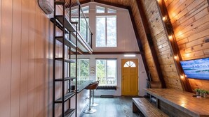 Ein modernes Loft-Zimmer mit hoher Decke, Holzbalken, einem großen Fenster, einer gelben Tür und einem Fernseher an der Wand.