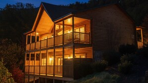 A two-story log cabin with a balcony, surrounded by trees. - Luxury 4 King Suites, 4 Bath Log Cabin Close to Town & Trolley (Gatlinburg)