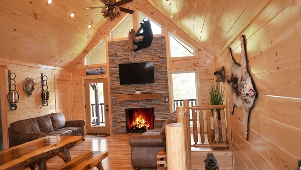 A cozy cabin interior with a stone fireplace, wooden walls, a leather sofa, and a dining table. - Luxury 4 King Suites, 4 Bath Log Cabin Close to Town & Trolley (Gatlinburg)