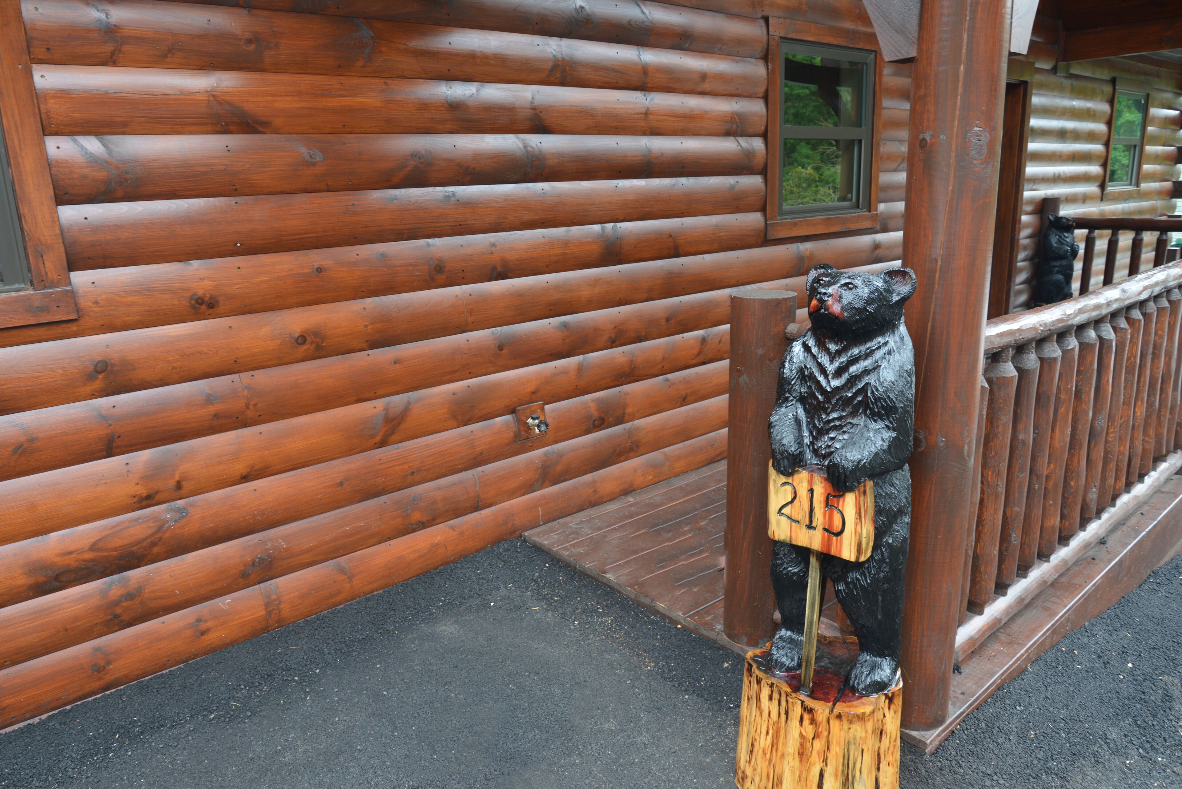 A wooden cabin with a bear statue holding a sign with the number 215.