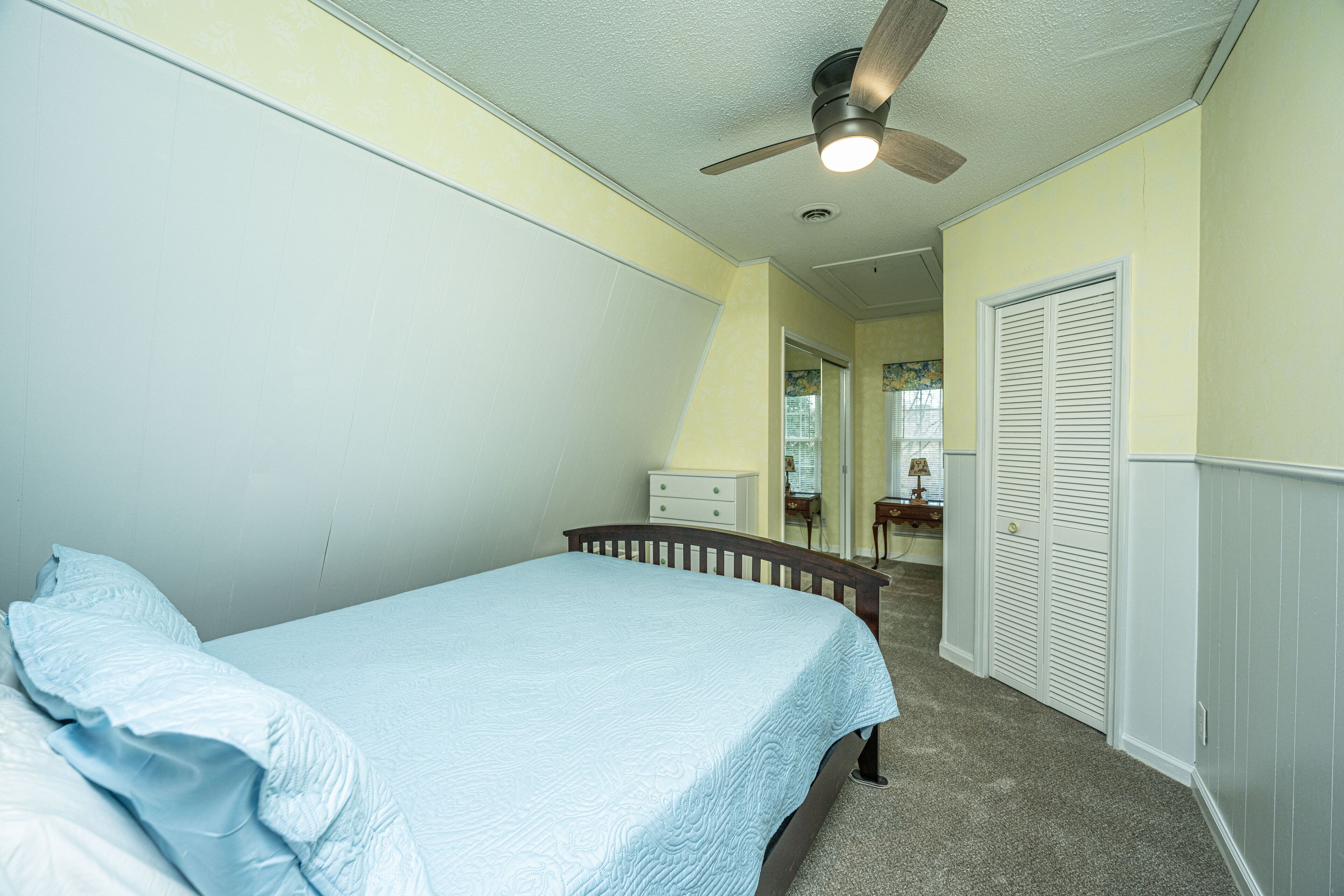 A bedroom with a bed, a ceiling fan, a dresser, and a closet.