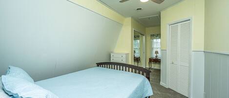 A bedroom with a bed, a ceiling fan, a dresser, and a closet.