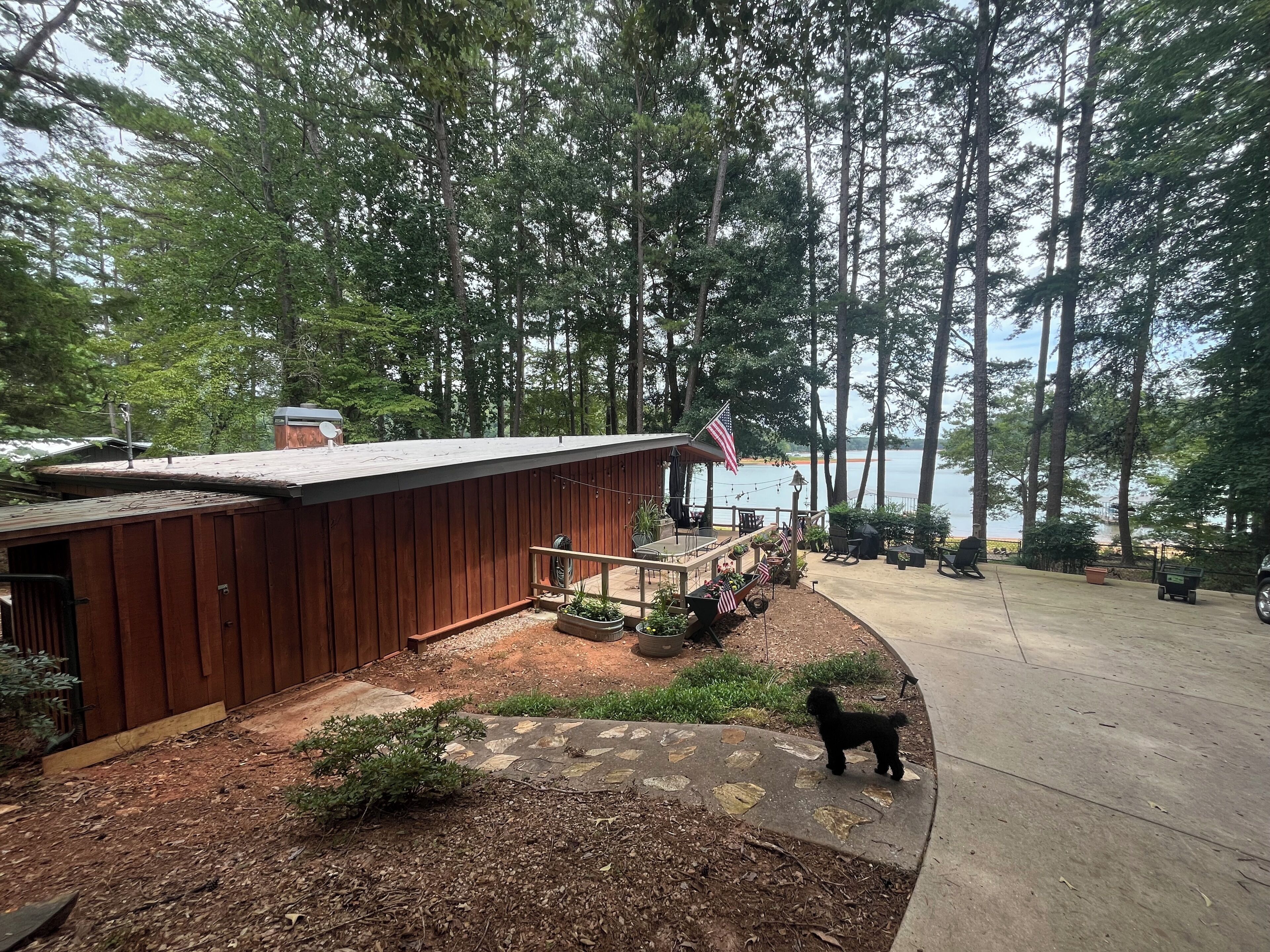 A wooden cabin with a deck overlooking a lake, surrounded by tall trees.