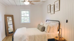 Een slaapkamer met een bed, een nachtkastje met een lamp, een raam en ingelijste botanische prints aan de muur.