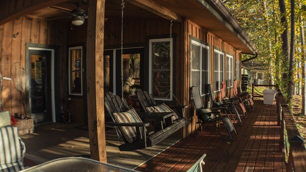 Een houten blokhut met een veranda, zitplaatsen buiten en uitzicht op bomen.