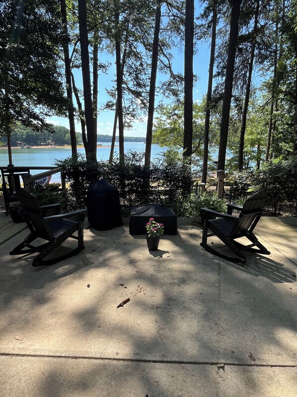 A patio with two rocking chairs and a small table, surrounded by trees and overlooking a body of water. - Contentment Cabin on Lake Hartwell (Martin)