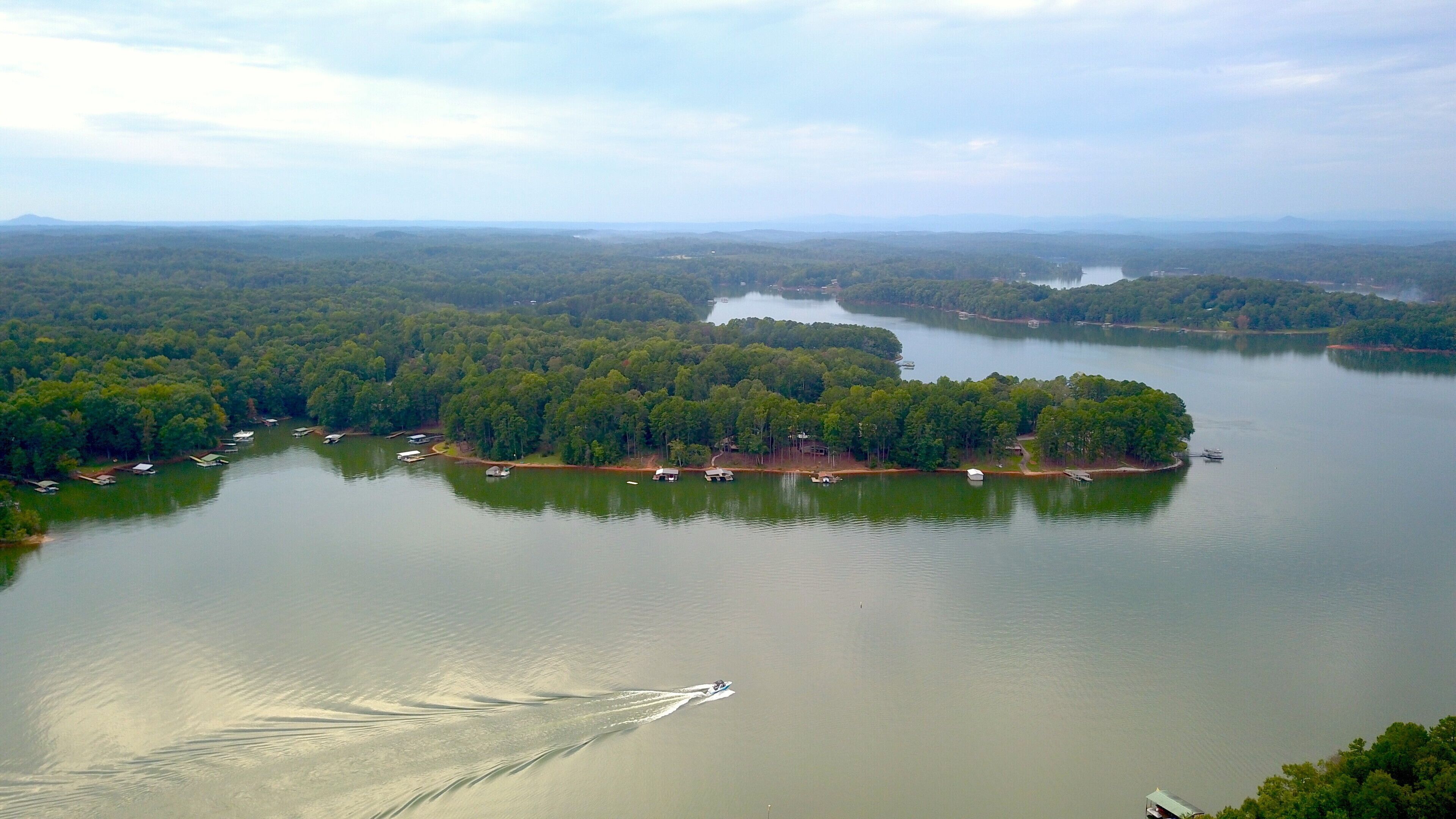 An aerial view of a lake surrounded by dense forest, with several docks and boats.