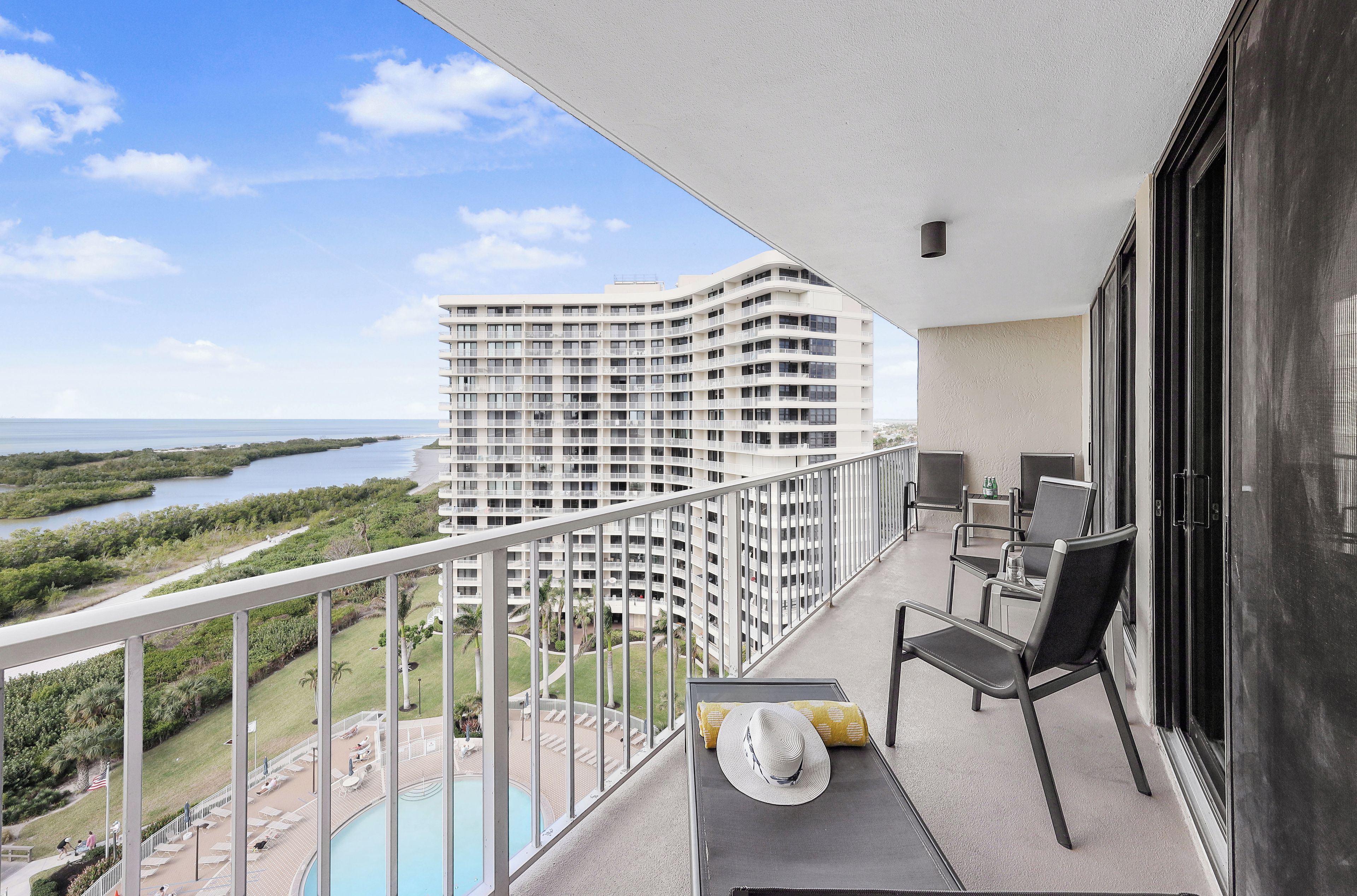 A balcony with a view of a large hotel building, a pool, and a natural landscape.