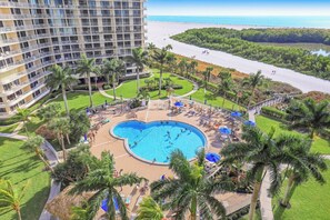 A hotel with a large pool, palm trees, and a view of the beach.