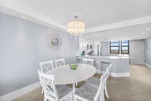 A modern kitchen with white cabinetry, a central island, and a dining area with white chairs.